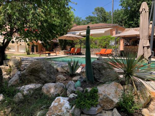 a swimming pool with an umbrella and some rocks at Ekin ô reV Gîte Fontessante in Montauroux