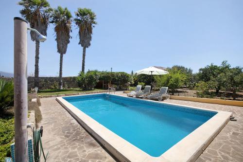 a swimming pool with palm trees and chairs and an umbrella at Las Tres Palmeras in Güimar