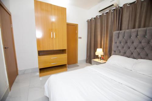 a bedroom with a white bed and a wooden cabinet at Oasis Villa Lekki in Lekki