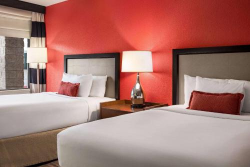 two beds in a hotel room with red walls at Ramada by Wyndham Albuquerque Airport in Albuquerque