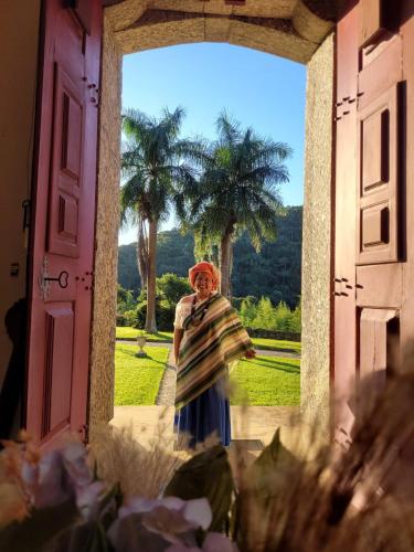 a woman standing in an open door with palm trees in the background at Fazenda Cachoeira Grande in Vassouras