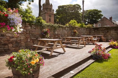 un gruppo di tavoli da picnic su una terrazza in legno con fiori di The Craster Arms Hotel in Beadnell a Beadnell