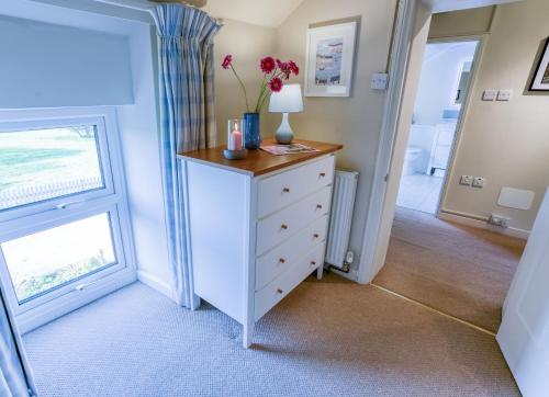 a room with a dresser with a lamp and a window at Tyn Lon in Moelfre