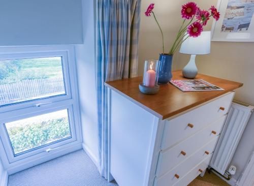 a dresser with flowers on it next to a window at Tyn Lon in Moelfre