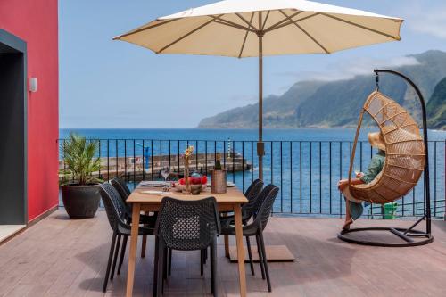 a table and chairs with an umbrella on a balcony at Holiday home by the sea Pipas do Avô - Seixal in Porto Moniz