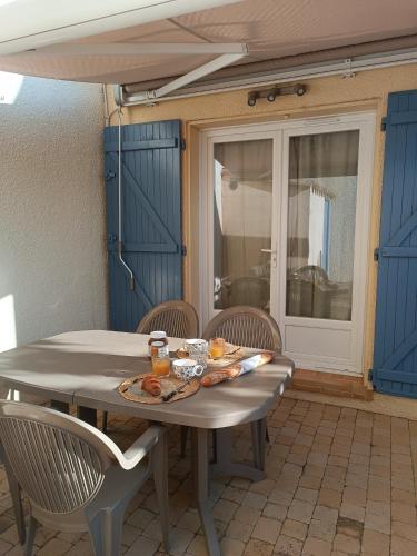 une table et des chaises dans une terrasse avec portes bleues dans l'établissement Le Charly, au Barcarès