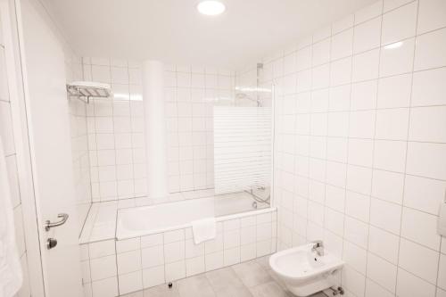 a white tiled bathroom with a tub and a sink at flexymotel Spielberg in Spielberg