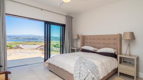 een slaapkamer met een bed en een groot raam bij Heron's View - lagoon views and solar power @Lake Brenton, Knysna in Knysna