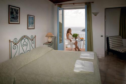 eine Frau auf einem Stuhl in einem Schlafzimmer mit einem Bett in der Unterkunft Hotel Sunset Green in Ischia