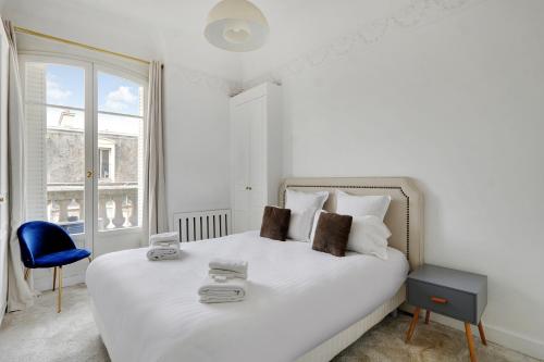 - une chambre blanche avec un grand lit blanc et une chaise bleue dans l'établissement Pick A Flat's Apartment in Montaigne - Cour Albert 1er, à Paris