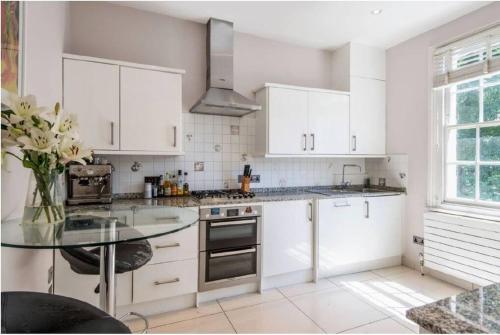a kitchen with white cabinets and a glass table at Stylish 2 FLOOR 2BED house 1 MIN walk to Camden station! FREE PARKING! in London