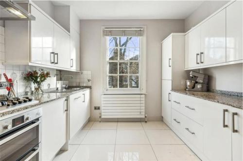 una cucina bianca con armadi bianchi e una finestra di Stylish 2 FLOOR 2BED house 1 MIN walk to Camden station! FREE PARKING! a Londra