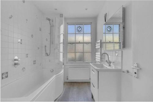 La salle de bains blanche est pourvue d'une baignoire et d'un lavabo. dans l'établissement Stylish 2 FLOOR 2BED house 1 MIN walk to Camden station! FREE PARKING!, à Londres