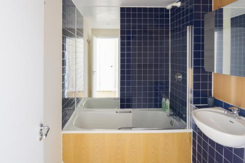 ein blau gefliestes Bad mit einer Badewanne und einem Waschbecken in der Unterkunft The Tower Bridge Cosy Flat in London