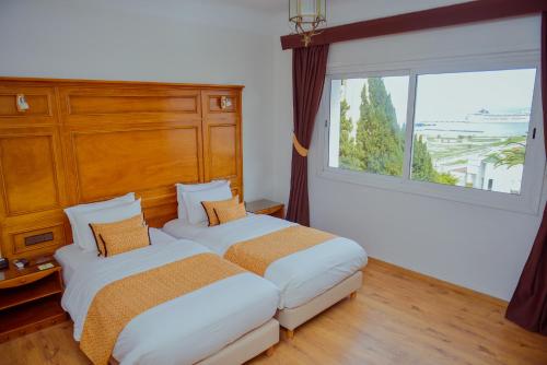 two beds in a room with a large window at Hôtel Rembrandt in Tangier