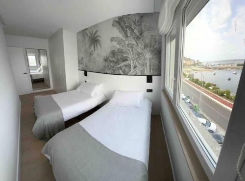two beds in a room with a large window at MALECON 47 Apartamento reformado en primera linea in Muxia