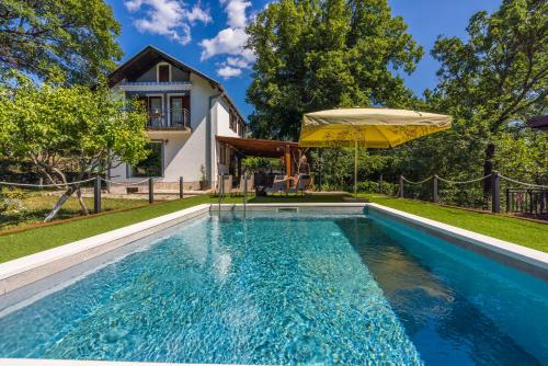 a swimming pool with an umbrella in front of a house at PLAVAC in Kostelj