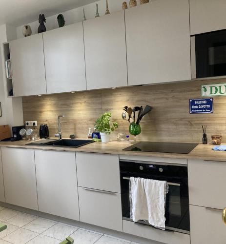 une cuisine avec des armoires blanches et un four noir dans l'établissement Bel Appartement avec balcon proche Roland Garos et Parc des Princes, à Boulogne-Billancourt