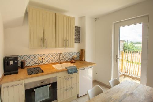 uma cozinha com armários brancos, um lavatório e uma mesa em Au coeur des champs em Nivelles