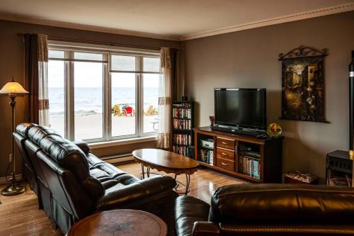 a living room with couches and a television with a view of the ocean at Les pieds dans le sable in Chambord
