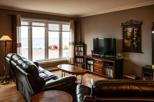a living room with a couch and a television with a view of the ocean at Les pieds dans le sable in Chambord