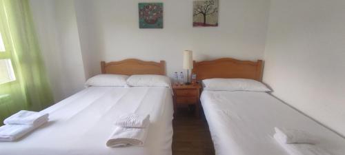 2 camas en una habitación con sábanas blancas y toallas en Apartamentos El Cruce, en Villafranca del Bierzo