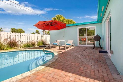 a swimming pool with a red umbrella and a house at Sun-Kissed Bliss: Dreamy Getaway in West Palm Beach