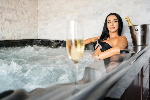 Backyard Jacuzzi House في أوراديا: امرأة في حوض استحمام ساخن مع كوب من الشمبانيا