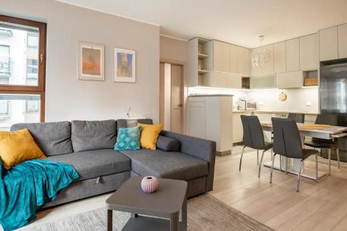 a living room with a gray couch and a kitchen at Woronicza Superb Place To Live Mokotow in Warsaw