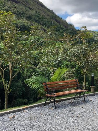 um banco de parque sentado em cascalho em frente a uma montanha em Pousada Sítio das Pedras em Domingos Martins