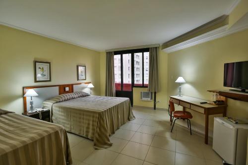 ein Hotelzimmer mit 2 Betten, einem Schreibtisch und einem TV in der Unterkunft San Michel Hotel in São Paulo