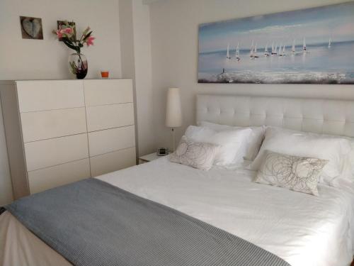 um quarto com uma cama branca e uma pintura na parede em Apartamento Lekeitio, Garaje y WIFI em Lekeitio