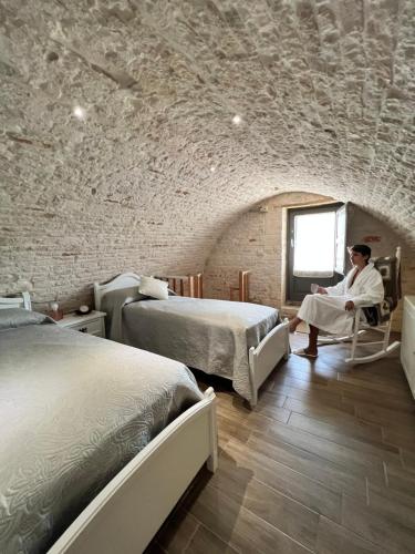 a man sitting in a chair in a room with two beds at Trulli MADIA Luxury Alberobello in Alberobello