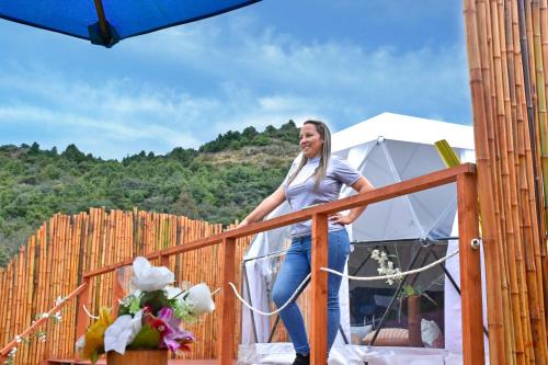 a woman standing on a wooden balcony next to a tent at Glamping Claro de Luna in Guatavita