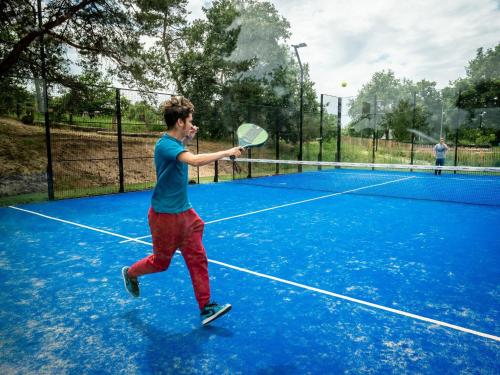 un homme tenant une raquette de tennis sur un court de tennis dans l'établissement Beautiful chalet with air conditioning in a holiday park on the Leukermeer, à Well