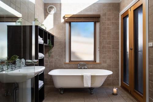 baño con bañera, lavabo y ventana en Ravenswood, en Daylesford