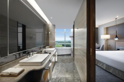 a bathroom with a sink and a tub and a bed at Grand Barony Qingdao Airport Hotel in Qingdao