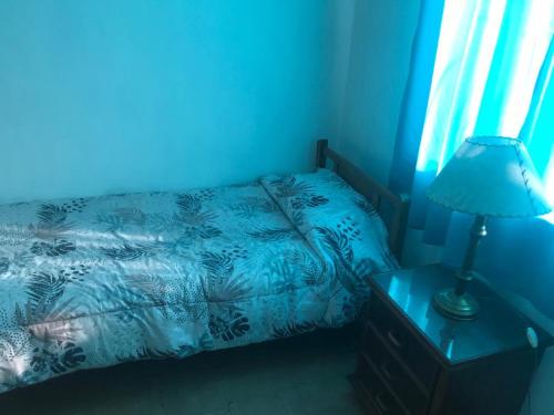 Dormitorio azul con cama y mesita de noche con lámpara en Family Hostel en Perito Moreno