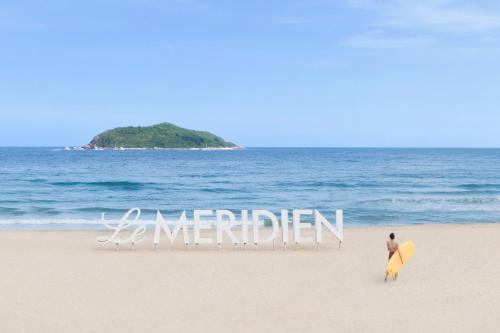 mężczyzna stojący na plaży z deską surfingową w obiekcie Le Méridien Shimei Bay Beach Resort & Spa w mieście Wanning