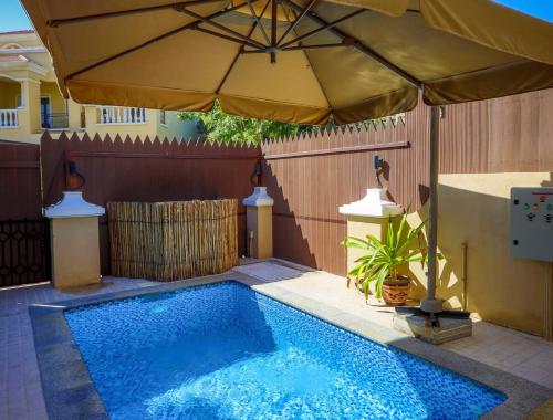 una piscina con sombrilla junto a una valla en Dar 66 Plunge Pool Resort Townhouses en Ras al-Khaimah