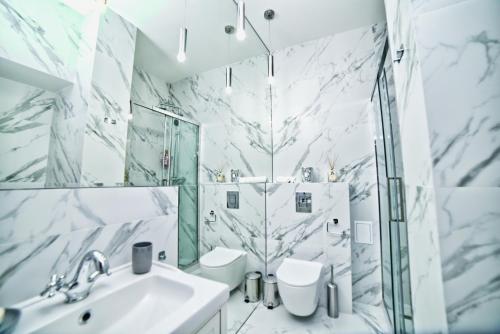 La salle de bains est pourvue de murs en marbre blanc, d'un lavabo et de toilettes. dans l'établissement Marszałkowska Move in Premium apartament no 1, à Varsovie