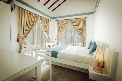 ein weißes Schlafzimmer mit einem Bett und zwei Fenstern in der Unterkunft The Beach house by Kay Jay Hotels in Pasikuda