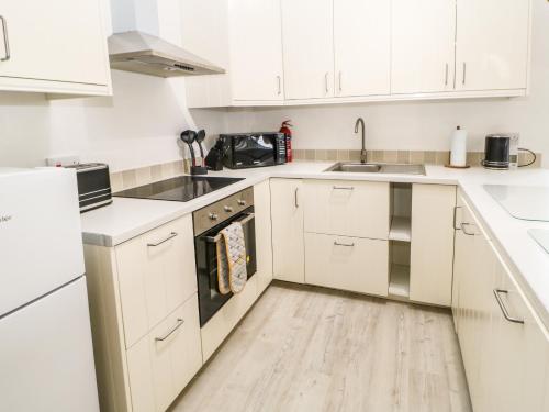 a white kitchen with white cabinets and a wooden floor at Whinstone in Keisley