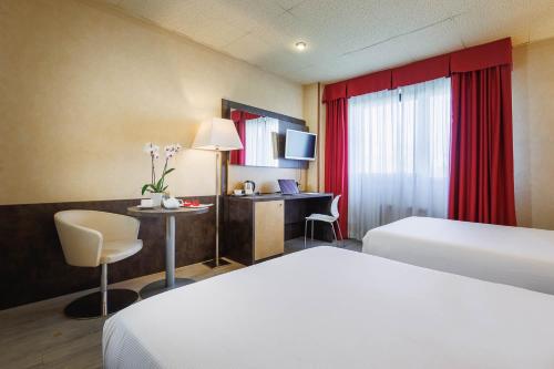 a hotel room with two beds and a desk at JR Hotels Bologna Amadeus in Bologna