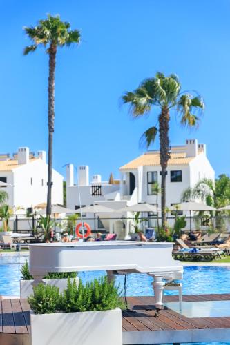 a white piano in front of a pool with palm trees at Apartamentos Honório - Vilamoura in Vilamoura