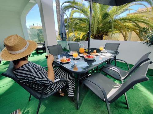 Eine Frau mit einem Hut, die an einem Tisch mit Essen sitzt. in der Unterkunft Aldeamento Praia dos Beijinhos in Porches