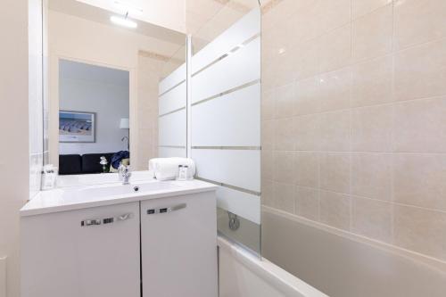 La salle de bains blanche est pourvue d'un lavabo et d'un miroir. dans l'établissement Résidence Goélia Green Panorama, à Cabourg
