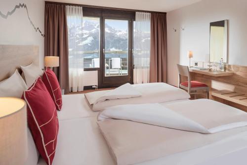 2 bedden in een hotelkamer met een bureau en een raam bij Dorint Blüemlisalp Beatenberg/Interlaken in Beatenberg
