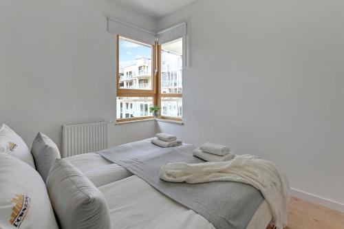 Ce lit se trouve dans un dortoir blanc doté d'une grande fenêtre. dans l'établissement Downtown Apartments Seaside Mila Baltica - Sauna, Gym & Parking, à Gdańsk