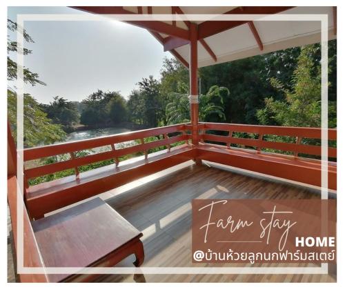 una terraza de madera con un banco y una sombrilla en บ้านห้วยลูกนกฟาร์มสเตย์ Banhuailuknok Farmstay en Ratchaburi